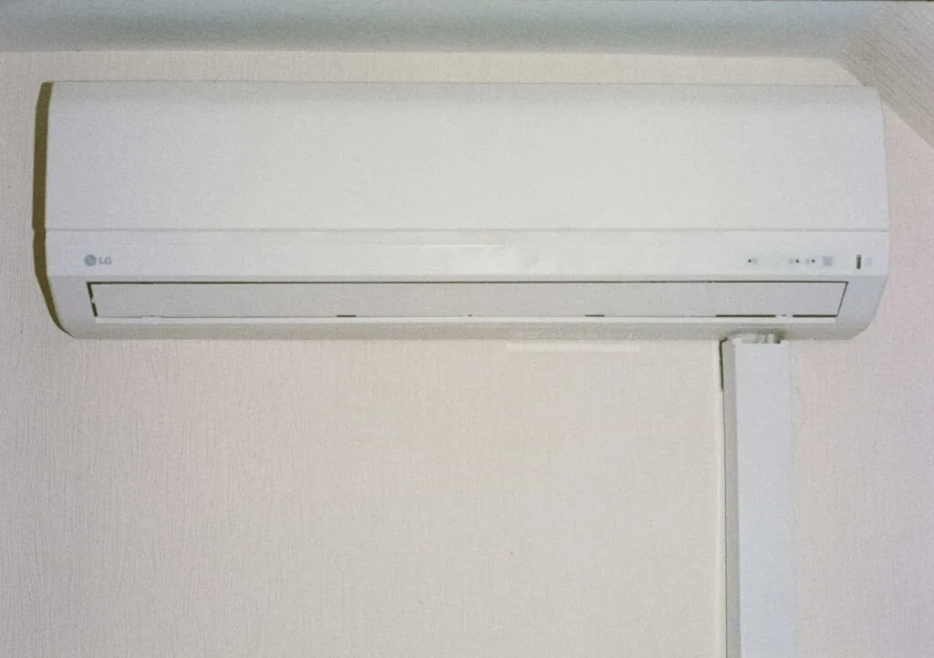 Wall-mounted white air conditioning unit with a vent at the bottom, installed on a light-colored wall.