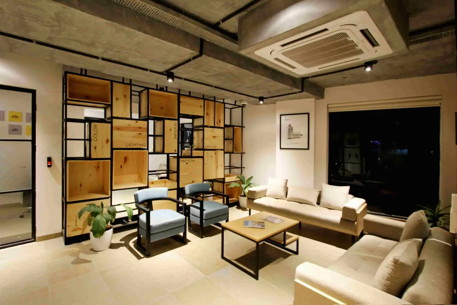 Modern office lounge with beige sofas, blue chairs, a wooden coffee table, potted plants, and a wooden shelving unit against a wall under ceiling air conditioning—highlighting how you can ensure year-round HVAC reliability in Greater Vancouver.