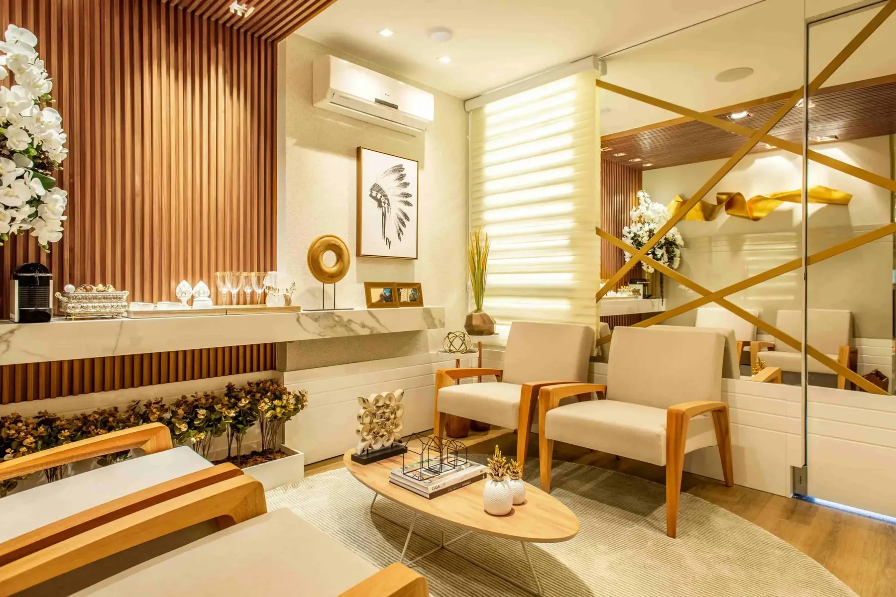 Modern waiting room with beige armchairs, a wooden coffee table, wall décor, indoor plants, and a mirrored accent wall with gold geometric lines—creating an inviting space to discuss topics like Why Does Duct Cleaning Boost Your HVAC Performance in Vancouver?.